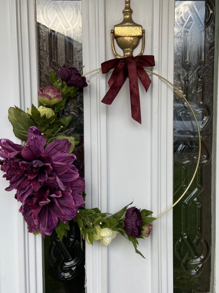 How To Make A Modern Christmas Wreath: A modern asymmetrical take on the traditional Christmas wreath styling different sizes of purple and white faux flowers asymmetrically around a gold hoop. A creative DIY modern wreath idea Christmas decor for you front door. @chloedominik #christmaswreaths #modernchristmaswreath #christmaswreathsdiy #christmaswreathideas #modernchristmaswreathdiy #asymmetricalwreath #asymmetricalchristmaswreath