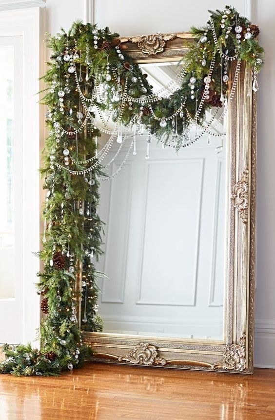 Christmas Garland Over Gilded Mirror: 9 Beautiful Christmas Flowers & Plants To Decorate With: A stunning home Christmas decoration idea using a garland draped over a gilded leaner mirror. The garland is styled with beautiful string crystals and pine cones balancing the natural and glamorous elements together. #christmasdecorations #christmasdecor #christmashomedecor #leanermirrordecor #gildedmirror #gildedmirrordecor #christmasgarland #christmasgarlandsideas